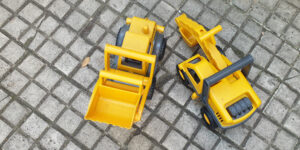 2 gelbe Spielzeugbagger auf Pflasterboden draußen Bau